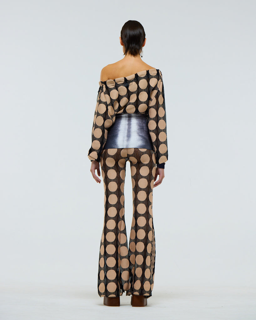 Model wearing a sheer stretch long sleeve black top with beige polka dot pattern, grey digital print muscle abs and adjustable drawstring neck on a plain background viewed from the back