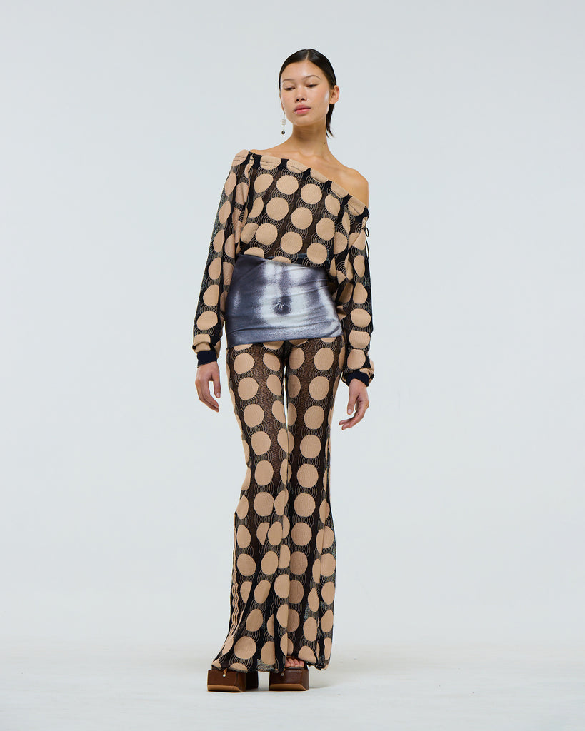 Model wearing a sheer stretch long sleeve black top with beige polka dot pattern, grey digital print muscle abs and adjustable drawstring neck on a plain background