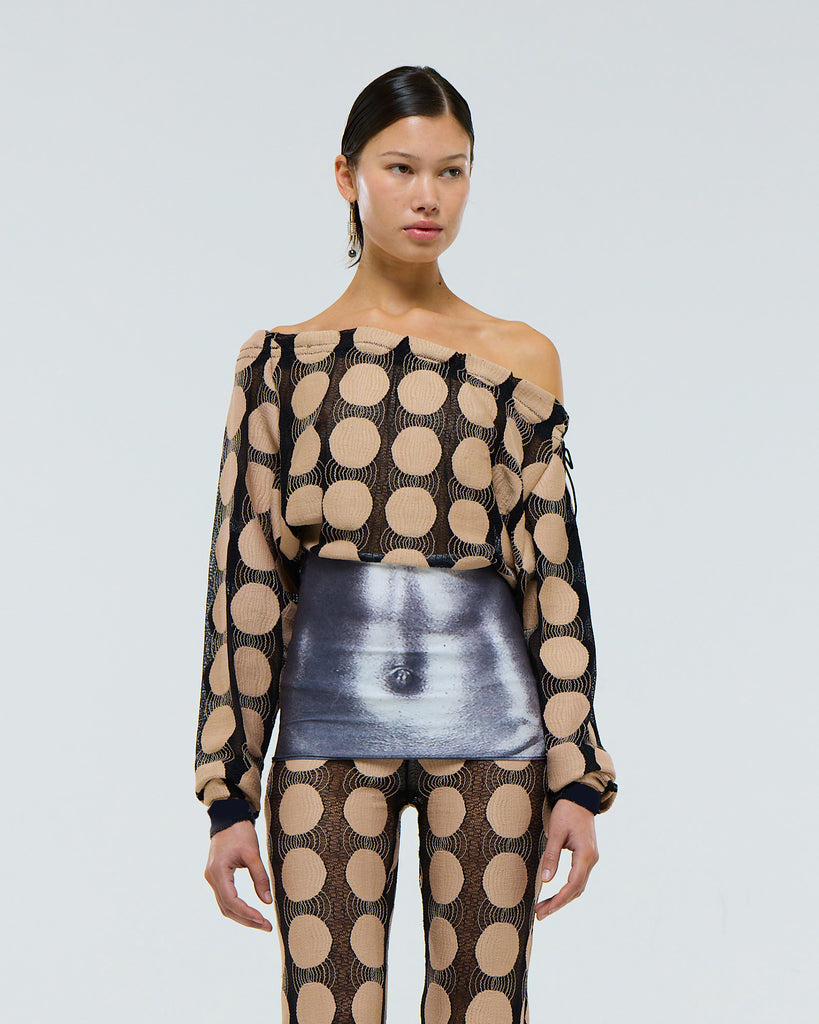 Model wearing a sheer stretch long sleeve black top with beige polka dot pattern, grey digital print muscle abs and adjustable drawstring neck on a plain background