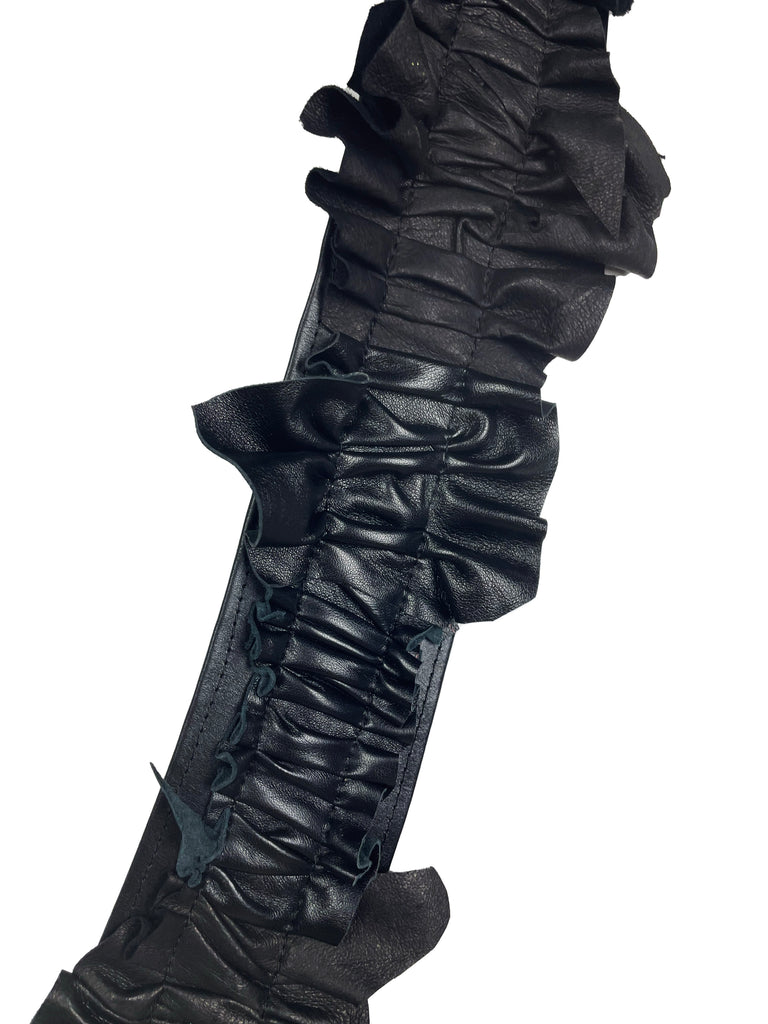 close up of ruffled black leather belt on a plain background