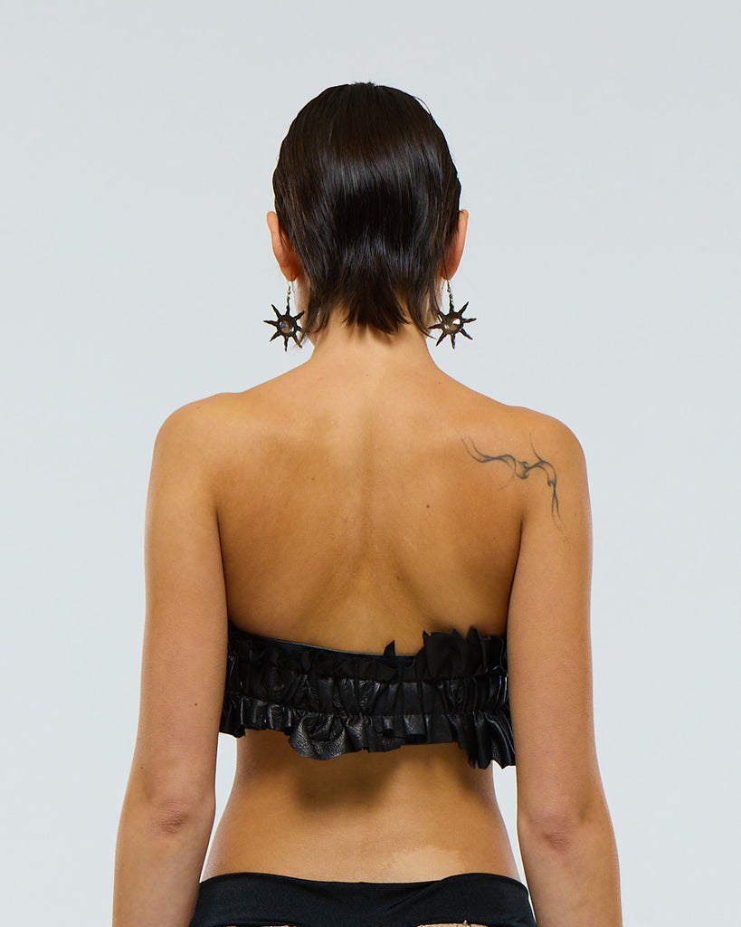 Model wearing a ruffled black leather belt with a very large silver aluminium frame shaped belt buckle on a plain background viewed from the back