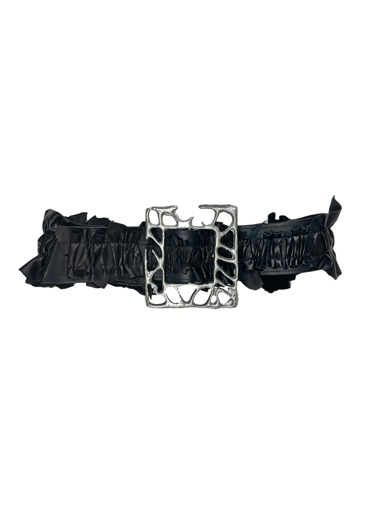 ruffled black leather belt with a very large silver aluminium organic frame shaped buckle on a plain background
