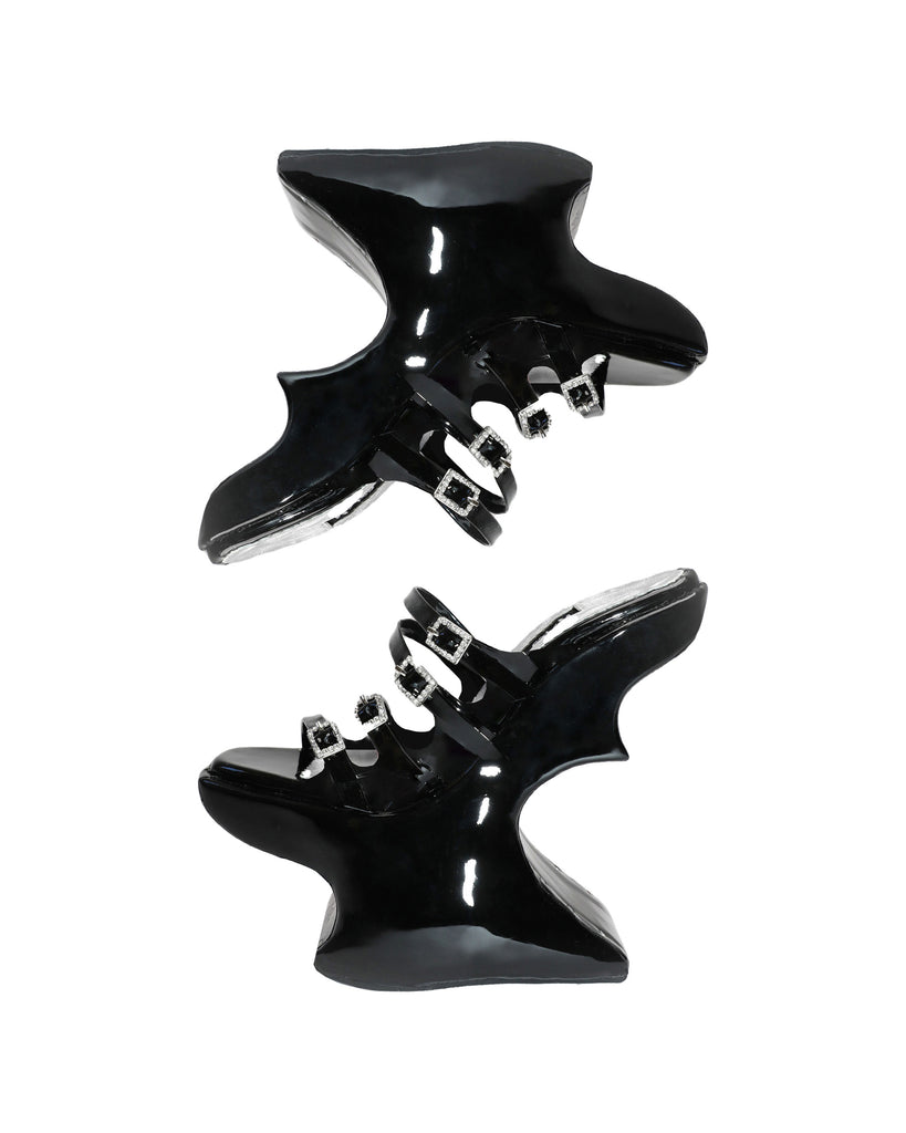 A pair of glossy black patent leather chopine platform shoes with silver toned buckles and details.