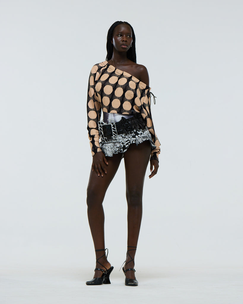 Model wearing a ruffled black leather belt with a very large silver aluminium frame shaped buckle and black and white skirt and spotted drawstring top on a plain background