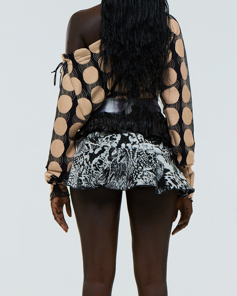 Model wearing a patterned top and black and white ruffled stretch abstract animal print skirt on a plain background viewed from the back