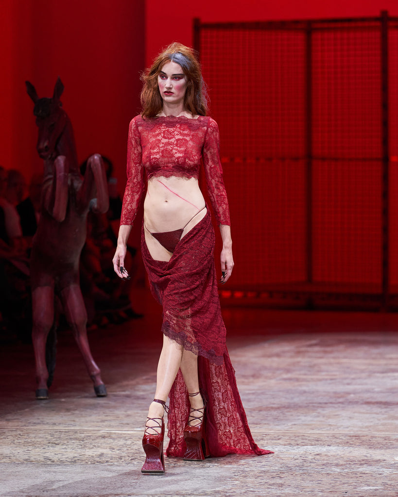 model on runway wearing red reptile print leather high heel chopine shoes with a platform sole and lace up front with exposed heel
