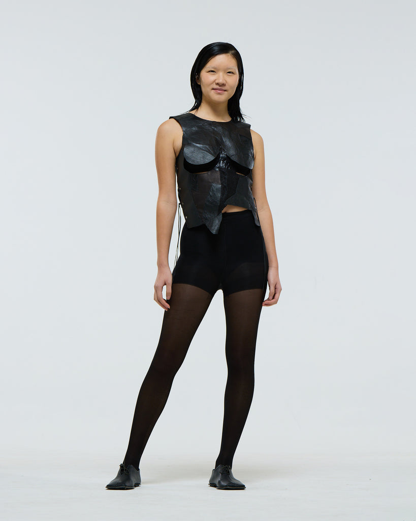 Model wearing a unique black leather patchwork sleeveless top made from salvaged leathers with under breast boob cut-outs on a plain background