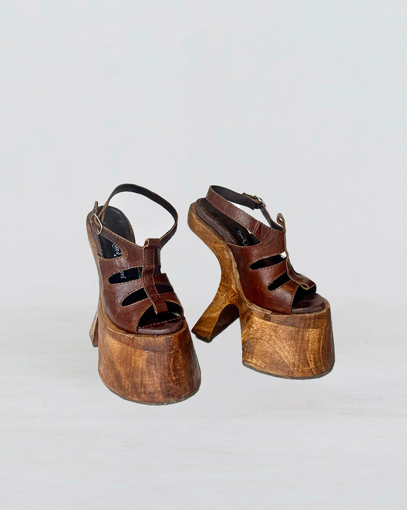 Pair of brown leather sandals with a wooden platform shaped like a horse hoof or hooves on a light gray background