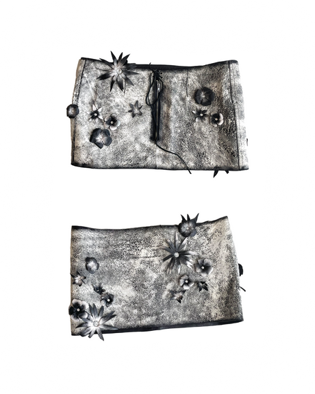 This image features a distinctive leather skirt adorned with hand-painted and formed leather flowers and rhinestone flower detailing. The rich, gray leather showcases a unique texture, and the skirt is designed with a low rise and a zip center back with lace-up detailing at the top.