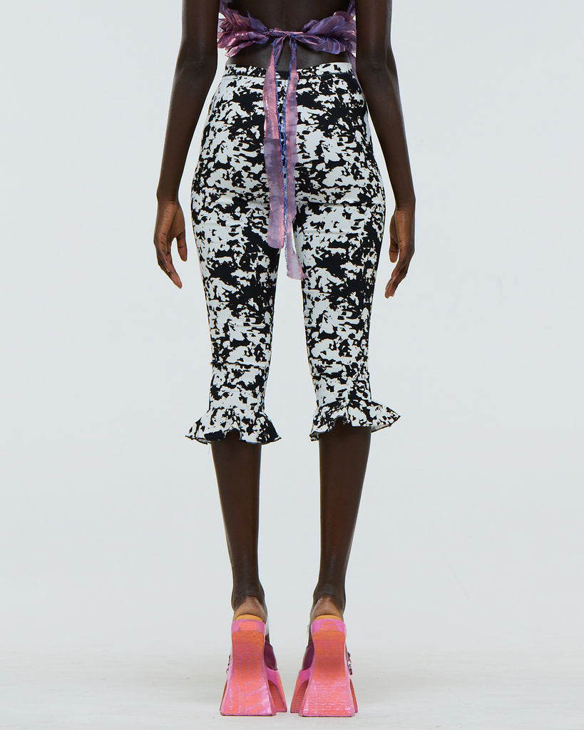 Model wearing black and white abstract patterned pants with a purple top on a white background viewed from the back