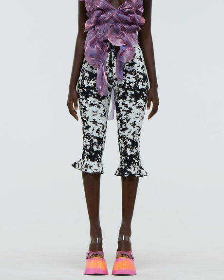Model wearing black and white abstract patterned pants with a purple ruffled top on a white background