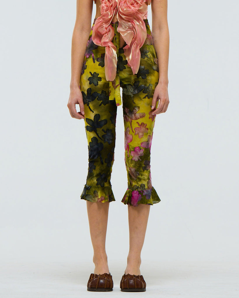 Model wearing tie dye floral capri pants with frill at the calf on a plain background