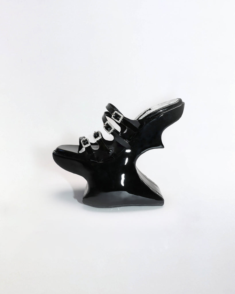 A pair of glossy black patent leather chopine platform shoes with silver toned buckles and details.