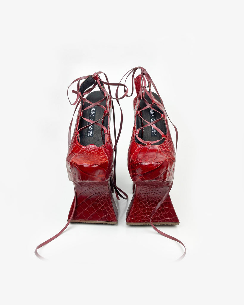 A red reptile print leather high heel chopine shoe with a platform sole and lace up front with exposed heel