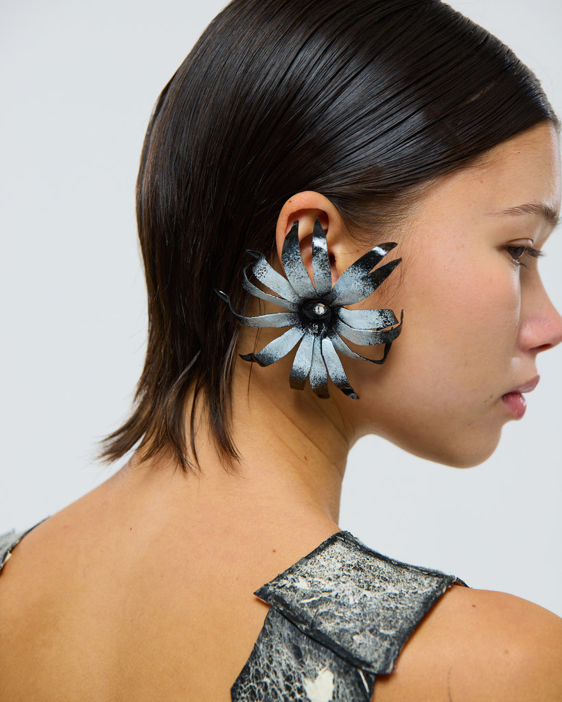 Model wearing a unique black and white floral cape daisy flower earring made from leather against a plain background