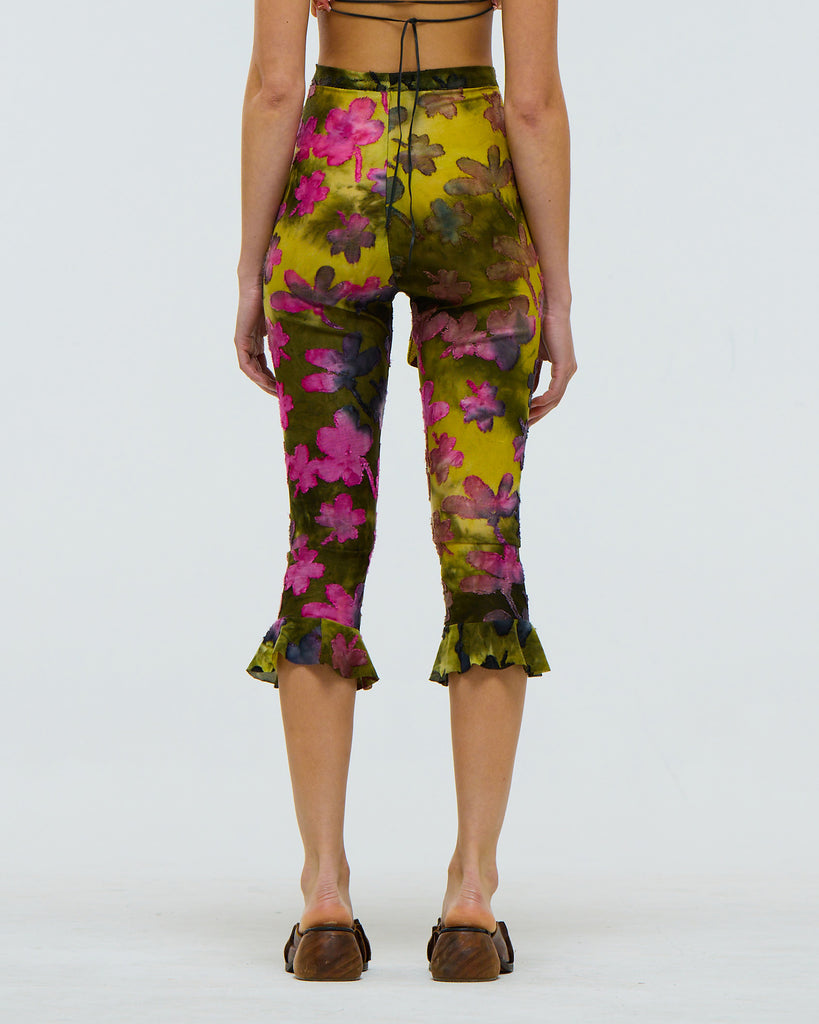Floral green and pink tie dye patterned capri pants worn by a model on a white background viewed from the back