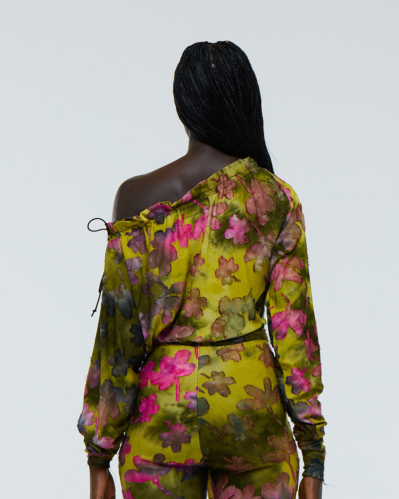 Model wearing a colourful green and pink floral tie dye patterned stretch long sleeve, drawstring neck top with high waist capri pants on a plain background viewed from the back