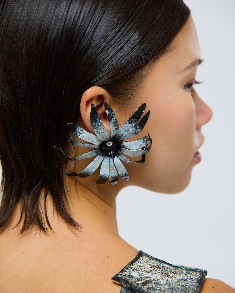 Model wearing a unique black and white floral cape daisy flower earring made from leather against with a rhinestone in the middle on a plain background