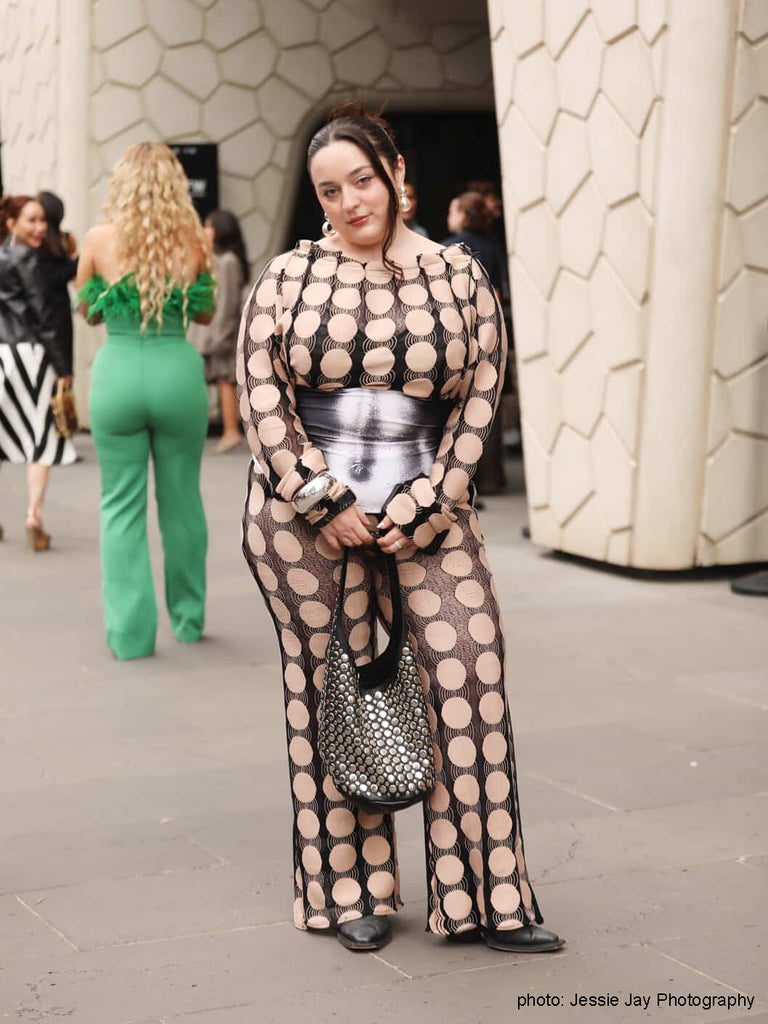 Person wearing a polka dot outfit with a metallic bag, standing outdoors.