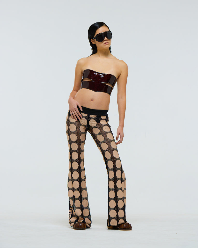 Model wearing a dark red burgundy patent leather strapless lace up top and patterned pants on a plain background