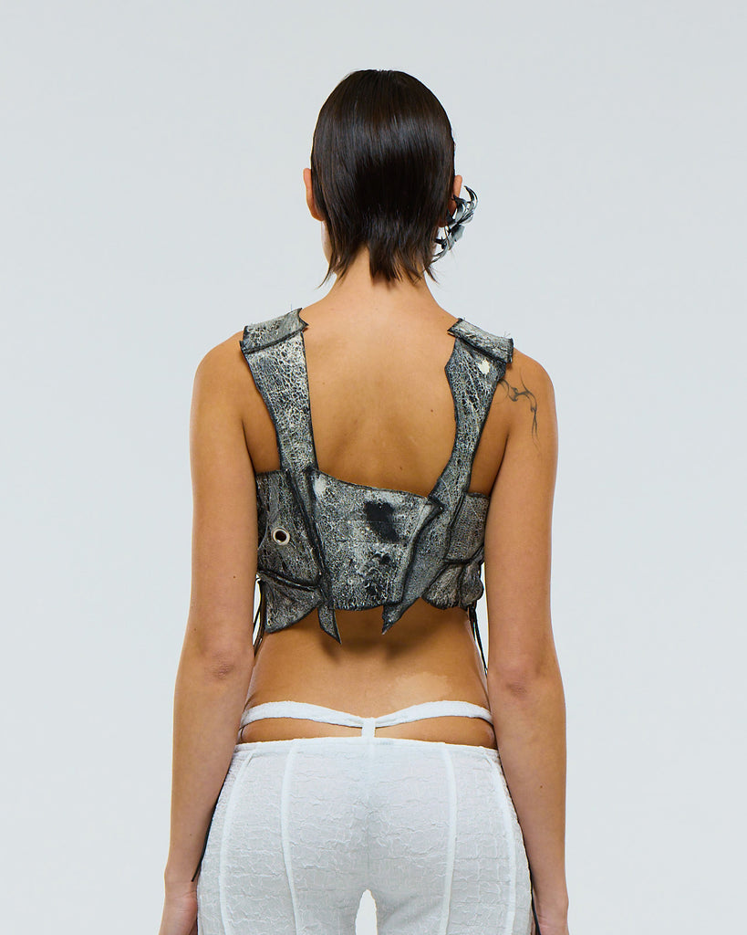 Model wearing a unique leather patchwork sleeveless top made from salvaged leathers on a plain background viewed from the back
