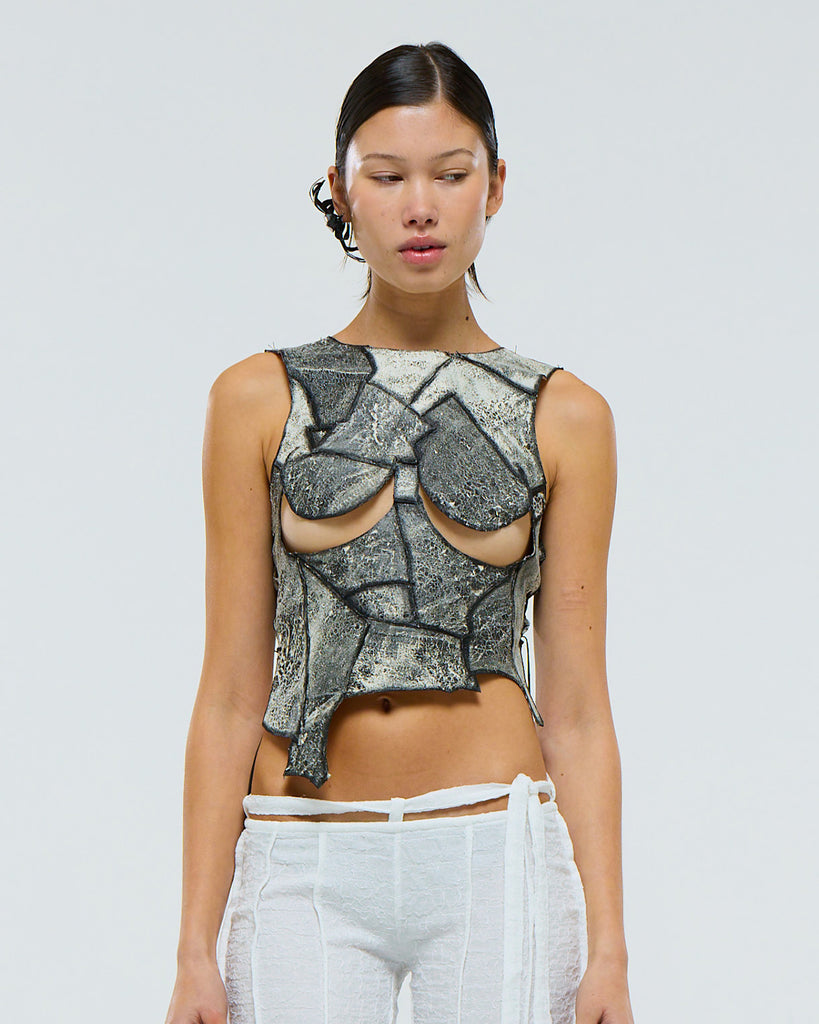 Model wearing a unique leather patchwork sleeveless top made from salvaged leathers with under breast boob cut-outs on a plain background