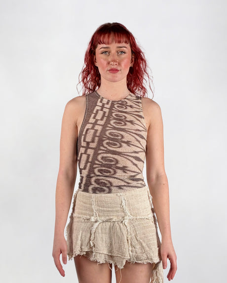 Woman wearing a sleeveless patterned mesh top and ruffled beige skirt on a white background