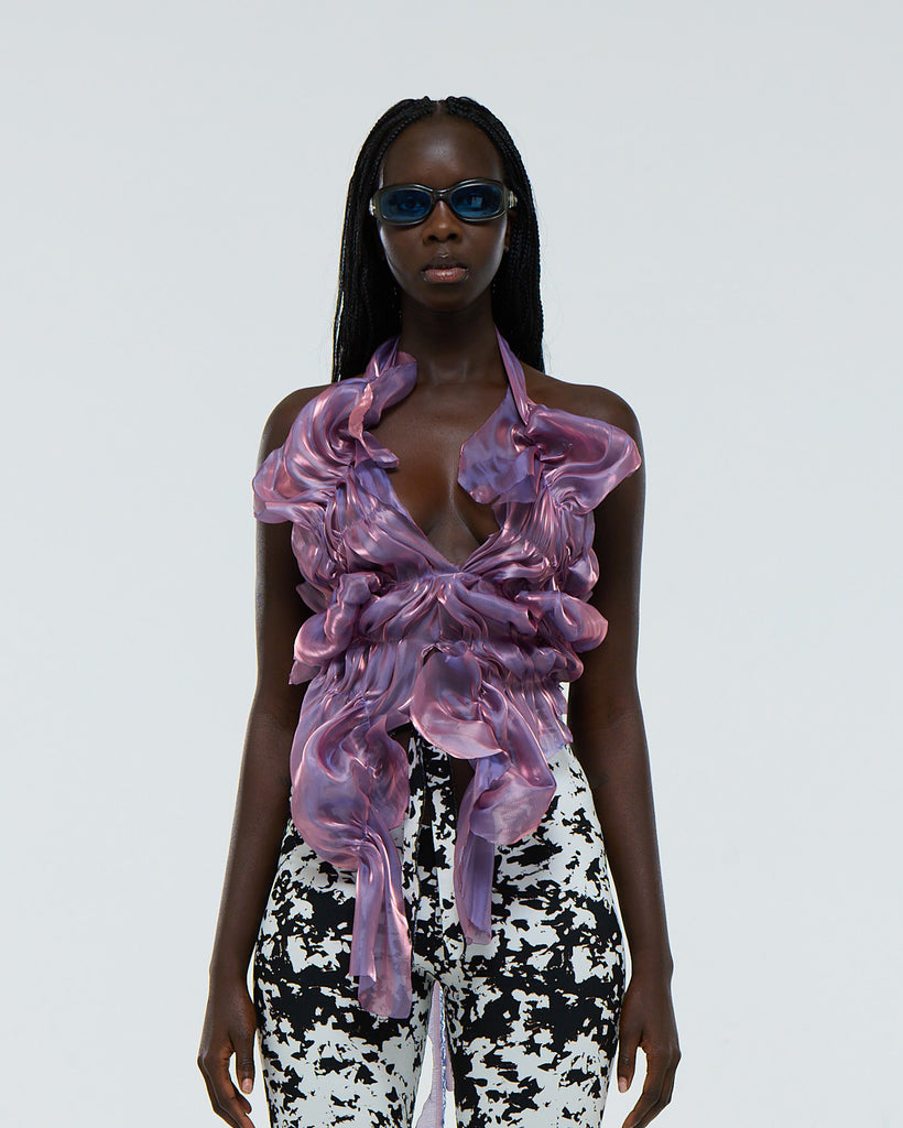 Model wearing a purple ruffled organza top and black and white patterned pants on a white background