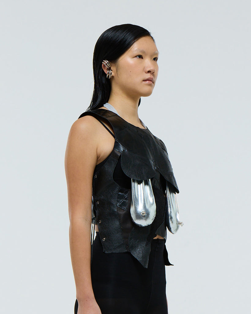 Model wearing a black sleeveless top with silver saggy breast boob bikini showing through on a plain background