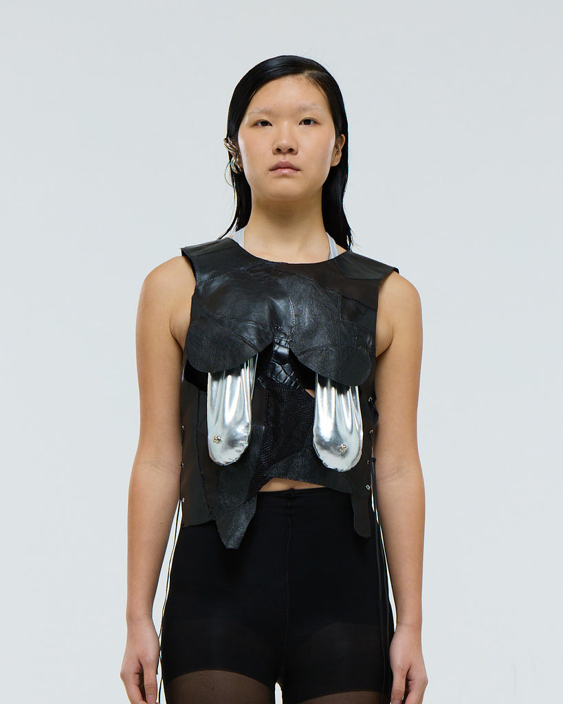 Model wearing a black sleeveless top with silver saggy breasts bikini on a plain background