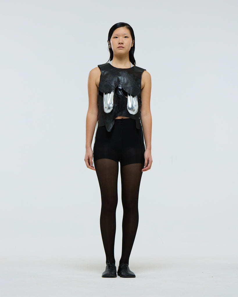 Person wearing a black sleeveless top with silver sagging decorative breasts on a plain background