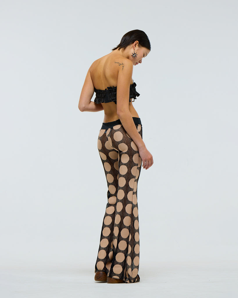 sheer black flared pants with beige polka dots worn by a model viewed from the side
