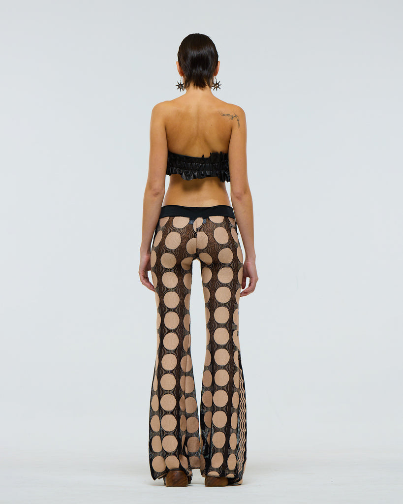 back view of model wearing sheer black flared pants with beige polka dot pattern against a white background