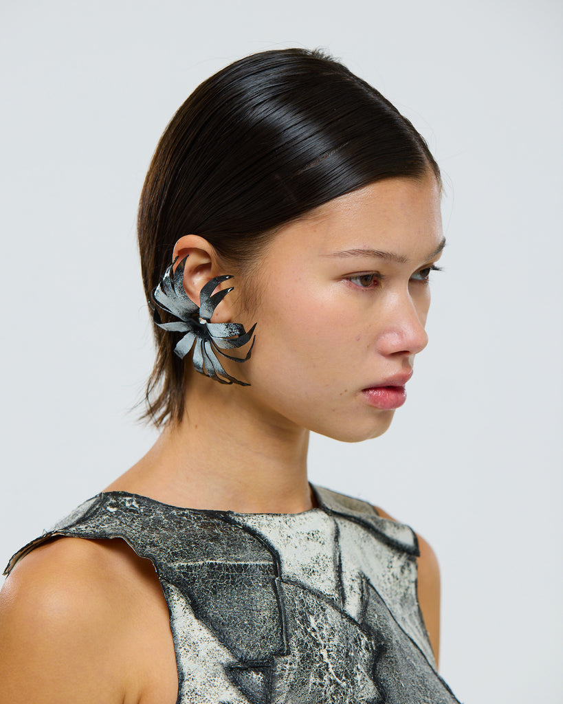 Model wearing a unique black and white floral cape daisy flower earring made from leather against a plain background