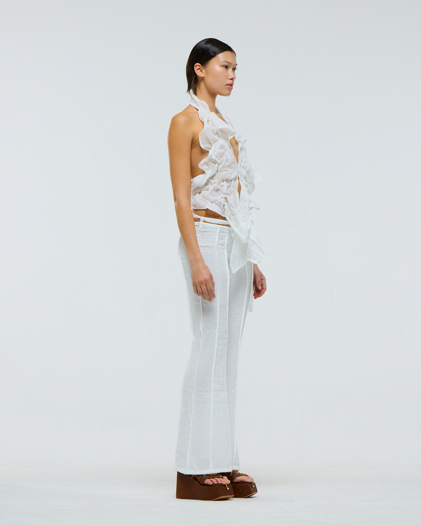 Model wearing a white ruffled linen top and white pants against a light gray background