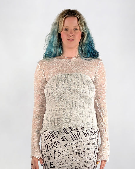 Person wearing a sheer white web like top over a text dress on a plain background
