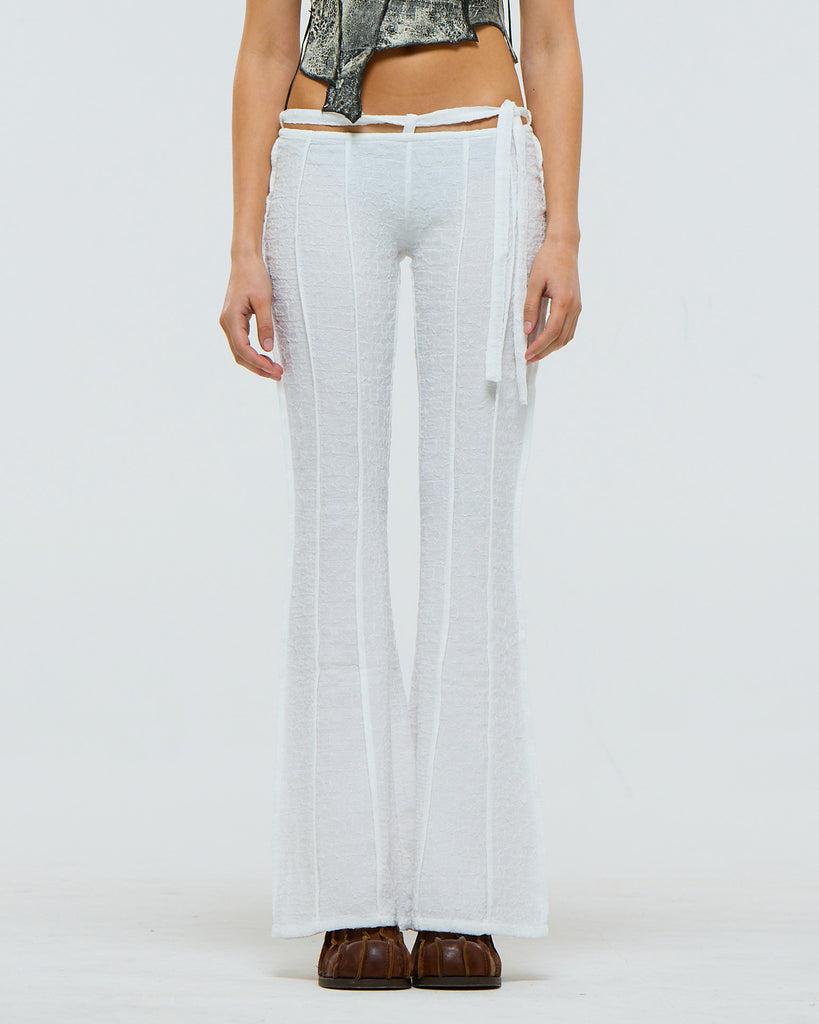 Model wearing white textured pants with horizontal french seams on a plain background